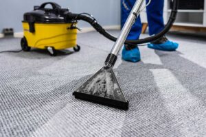 Person vacuuming floors while another wipes detailed kitchen surfaces in a bright home.